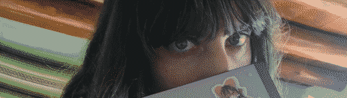 a pale dark haired girl with green eyes peeks over the edge of a computing device at you